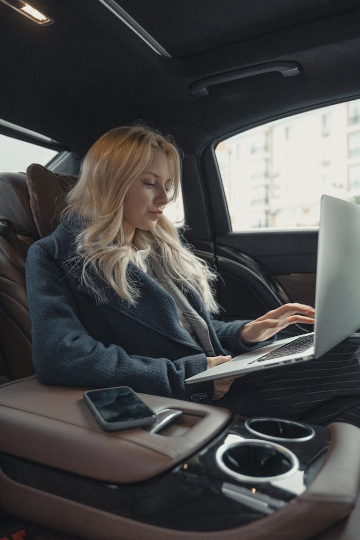 our-services-2 Businesswoman working remotely on a laptop in the backseat of a luxury car. Stylish, modern, and focused.